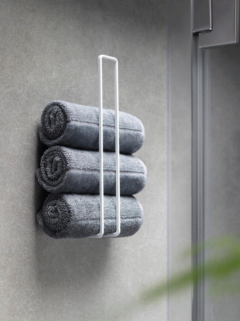 Idéal également comme porte-serviettes élégant pour les invités. Trois serviettes grises soigneusement empilées dans un porte-rouleau de papier toilette design blanc.