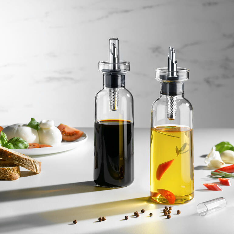 Ensemble de verseurs d'huile et de vinaigre avec un verseur décoratif et des ingrédients frais sur une table.