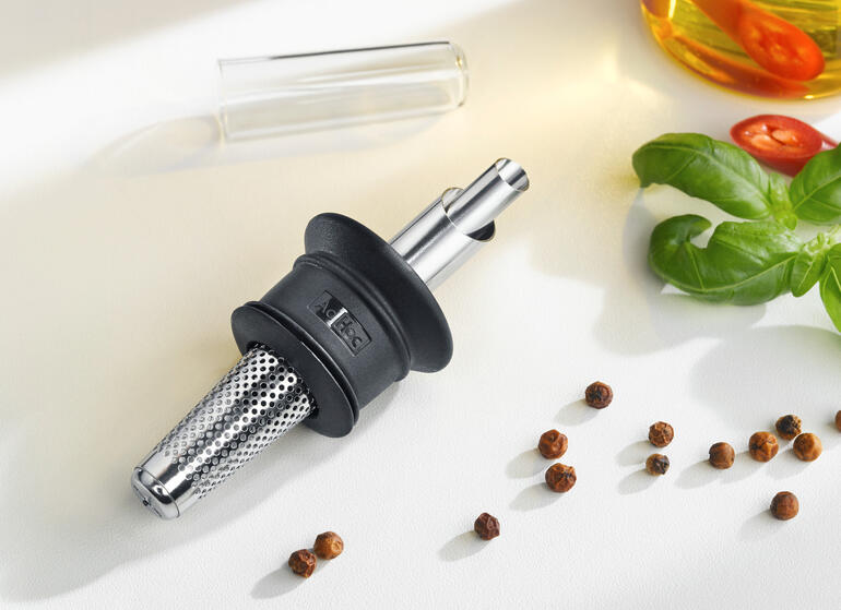 4 fois plus pratique : le bec verseur multifonction dose, filtre, retient les gouttes et se ferme hermétiquement pour préserver les arômes. Verseur décoratif pour huile et vinaigre sur une surface blanche avec des ingrédients.