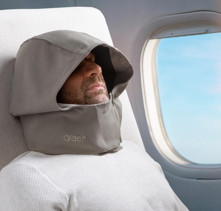 Homme avec un coussin de voyage et une capuche qui dort dans l'avion.