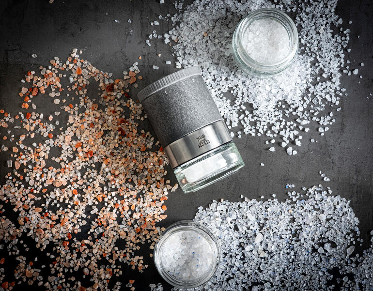 Ensemble de moulins à sel Peugeot Zirkonia sur une table avec du sel