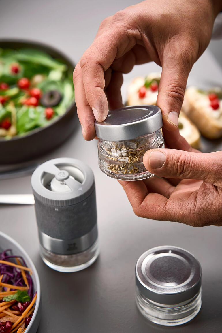 Ensemble de moulins à sel Peugeot Zirkonia, mains tenant un pot d'épices au-dessus d'un saladier