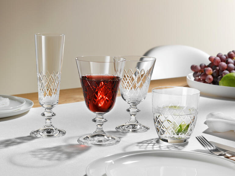 Deux verres au design Eaton sur une table, entourés de raisins et d'une table dressée.