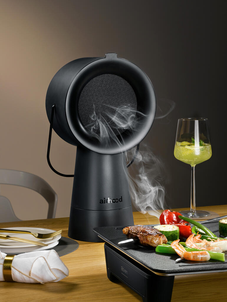 Airhood 2.0 en noir, appareil à griller fumant sur une table avec légumes et viande.