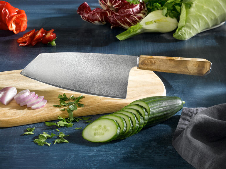 Couteau Nakiri en damas sur une planche en bois, entouré de légumes frais.