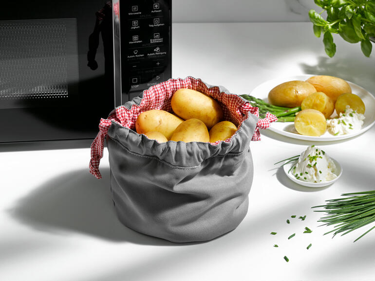 Sac à pommes de terre gris avec des pommes de terre et des herbes sur la table.