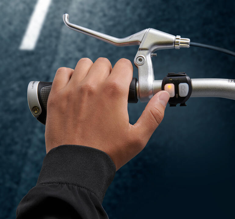 Casque vélo à signal lumineux Main appuyant sur le bouton du signal lumineux sur le guidon du vélo