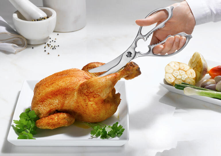 Ciseaux de cuisine et de volaille 2-en-1 coupant un poulet sur une assiette.