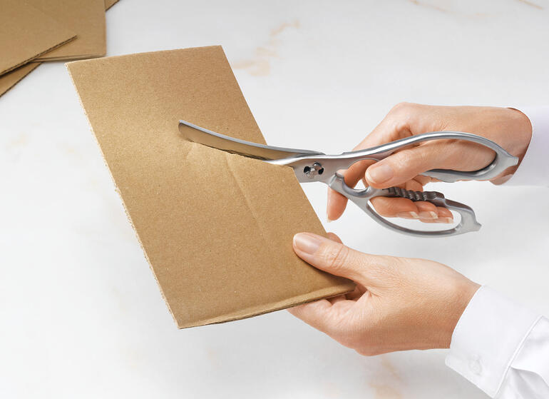 En même temps, également des ciseaux de cuisine multifonctions. Ciseaux de cuisine et de volaille 2-en-1 coupant à travers du carton marron.