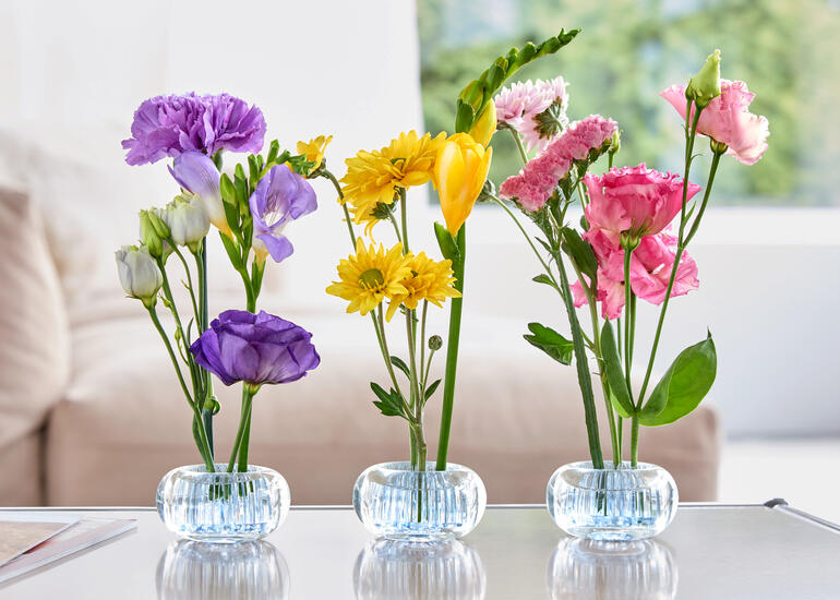 Trois mini-vases avec des fleurs colorées sur une table.