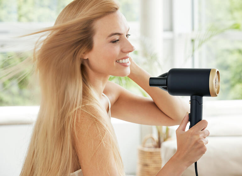 Sèche-cheveux de voyage compact en utilisation, femme en train de sécher ses cheveux.