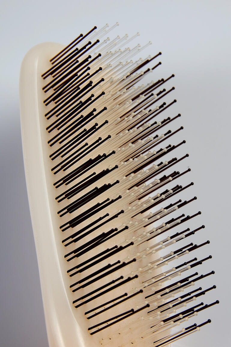 Gros plan d'une brosse à cheveux avec des épingles de protection sur fond blanc.