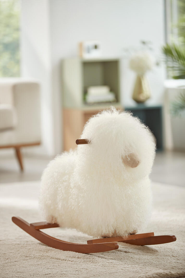 Bébé en peluche en peau de mouton blanche sur un tapis.
