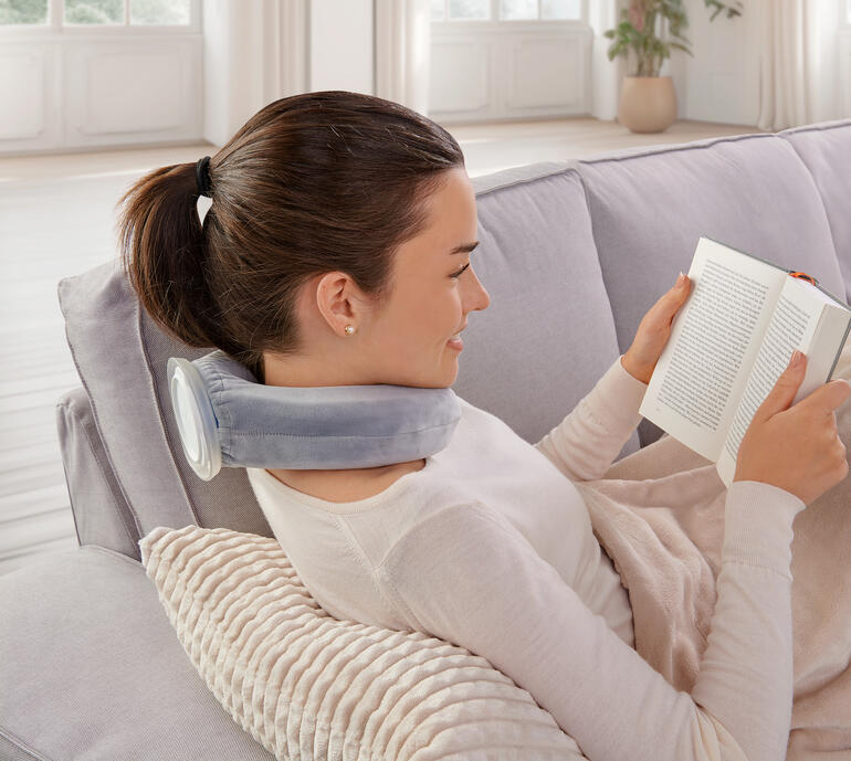 Femme avec un coussin chauffant lit un livre sur un canapé