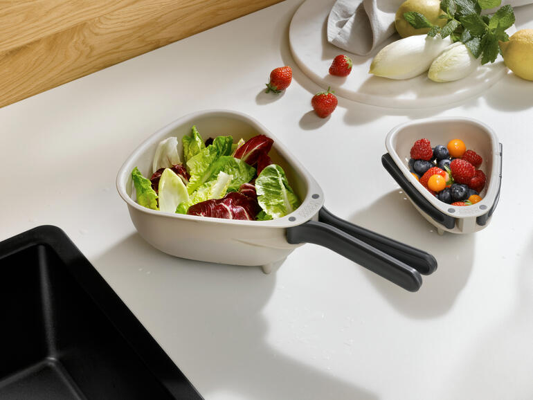 Passoire de cuisine compacte avec des légumes et des fruits frais en arrière-plan.