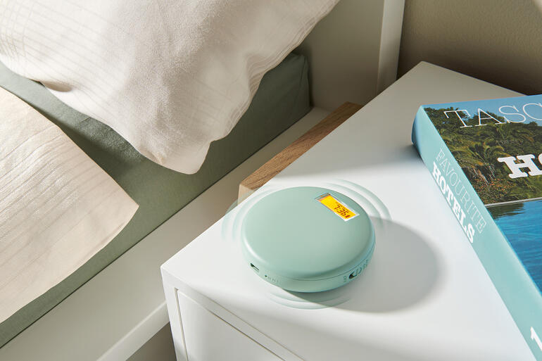 Réveil vibrant en vert doux, sur une table de nuit à côté d'un livre et d'une couette.