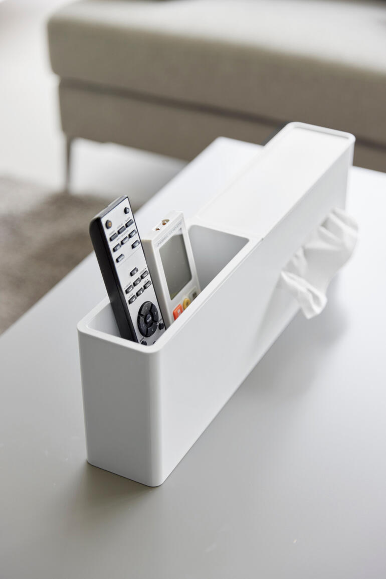 Boîte de mouchoirs blanche avec une télécommande et un smartphone sur une table.