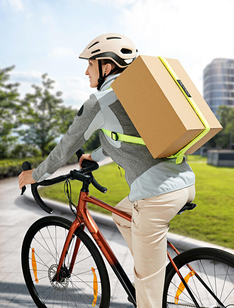 Homme à vélo avec un sac à dos pour colis transportant un grand paquet.