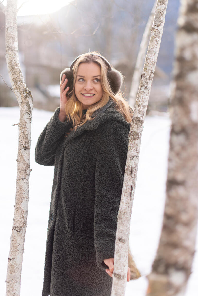 Femme avec des écouteurs en alpaga devant des bouleaux dans la neige.