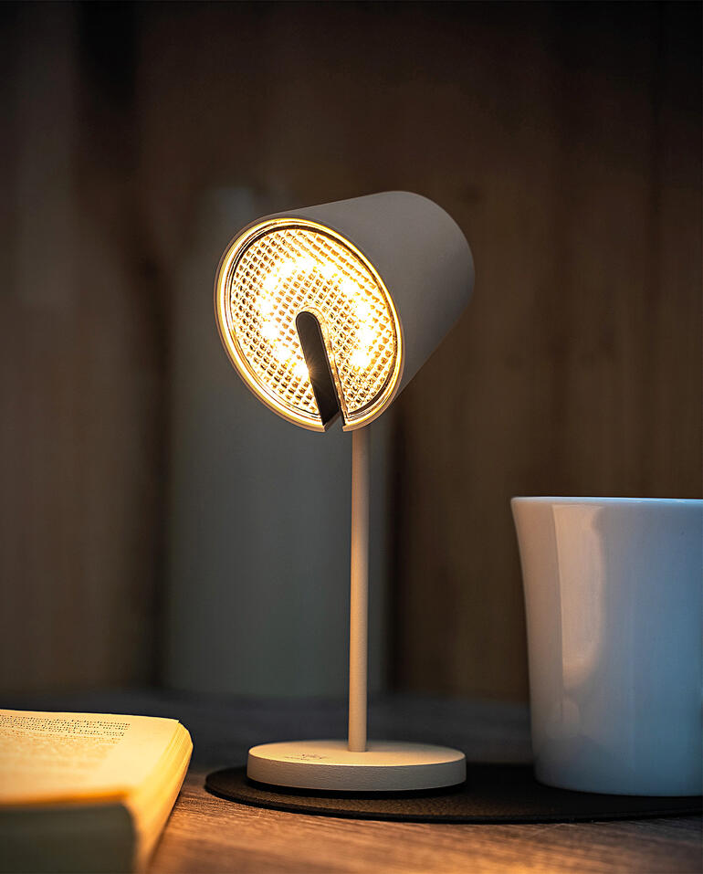 Lampe magnétique noire avec lumière claire, posée sur une table à côté d'une tasse.