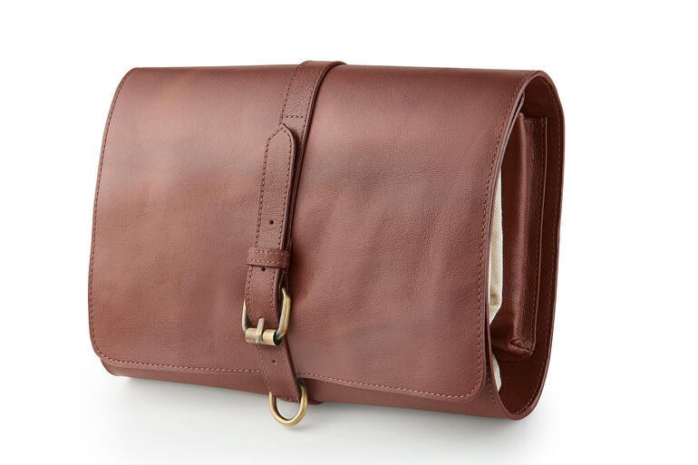 La boucle vous permet d’enrouler la trousse de toilette et de la maintenir parfaitement fermée. Trousse de toilette en cuir de buffle fermée avec boucle, sur fond blanc.