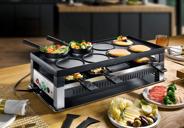 Appareil Solis raclette et fun-cooking 5-en-1 avec légumes et viandes sur la table.