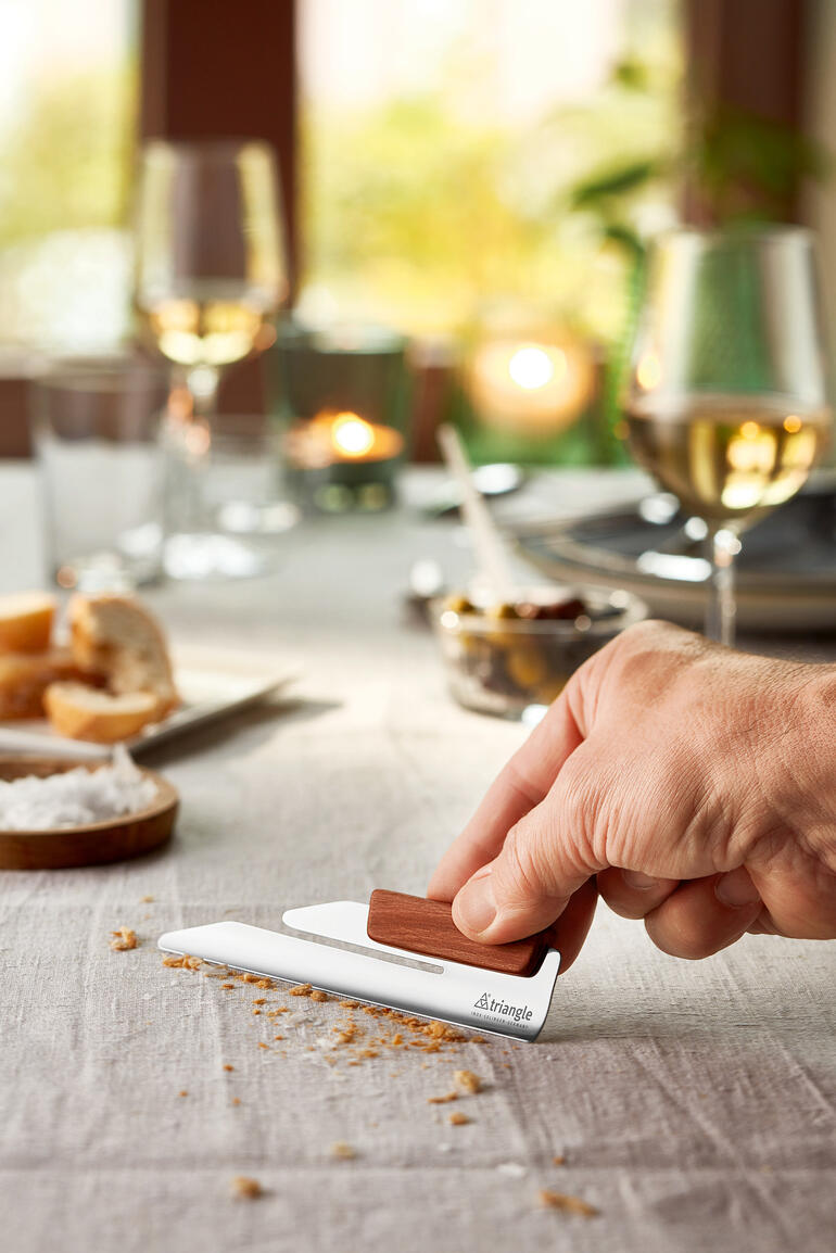 Main montrant le ramasse-miettes design sur une table dressée avec des collations.