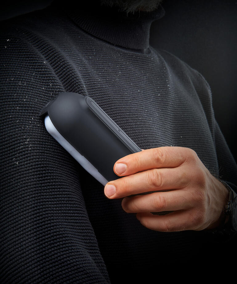 Rouleau adhésif ultra-collant dans la main d'un homme, avec des peluches sur un pull.