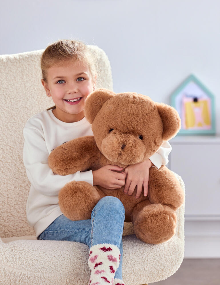 Fille avec un ours en peluche brun qui peut jouer un message vocal personnalisé.