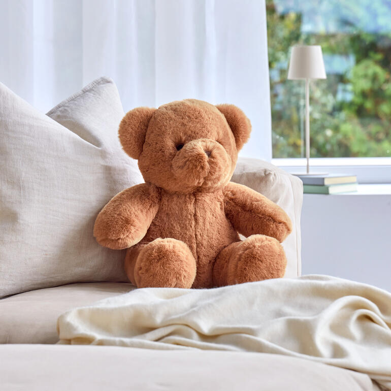 Ours en peluche brun sur un canapé confortable, prêt à être câliné.