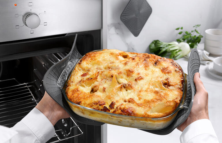 Une personne tient un plat à gratin avec un plat doré sortant du four, manique en silicone en usage.