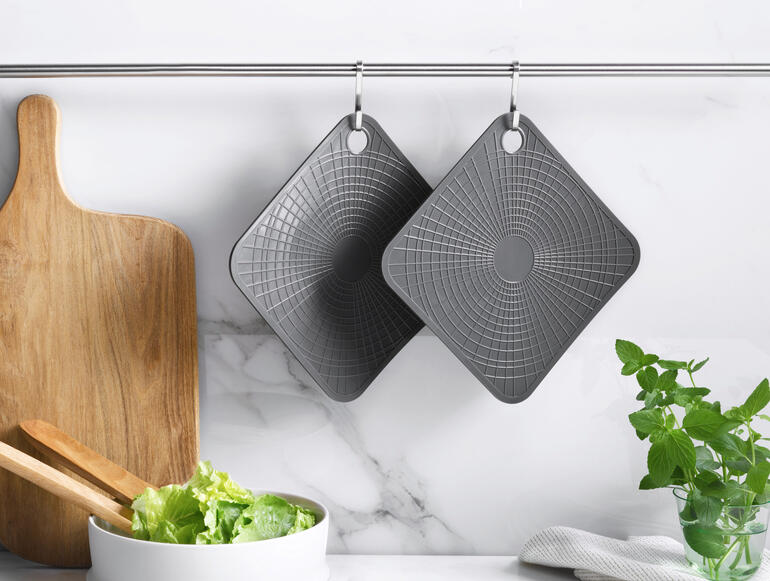 Deux gants de cuisine en silicone gris suspendus à une barre dans une cuisine moderne.