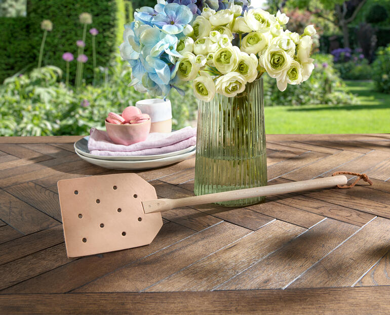 Fouette à mouches en cuir posée de manière décorative sur une table en bois rustique.