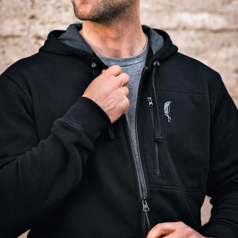 Homme en hoodie noir ferme une fermeture éclair et sourit légèrement.