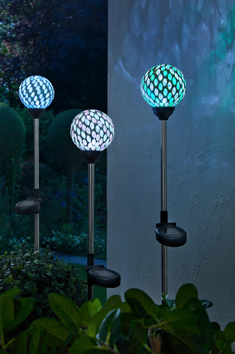 Trois piquets solaires avec des lampes en mosaïque colorées dans le jardin.