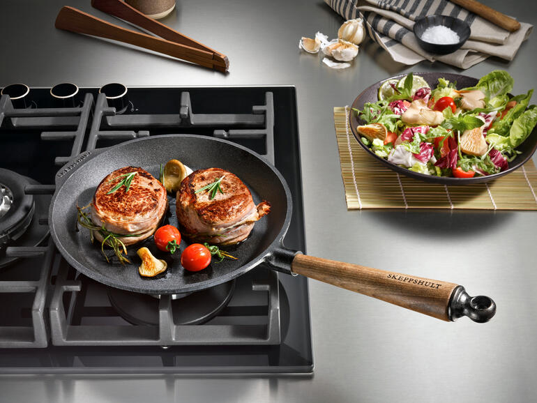 Poêle en fonte sur la cuisinière avec de la viande et des légumes frits