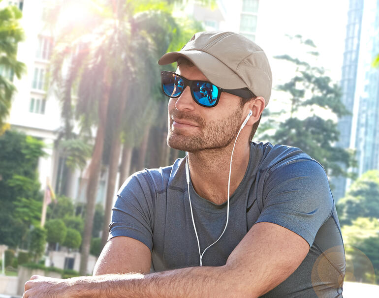 Homme avec casquette de refroidissement beige et lunettes de soleil assis à l'extérieur