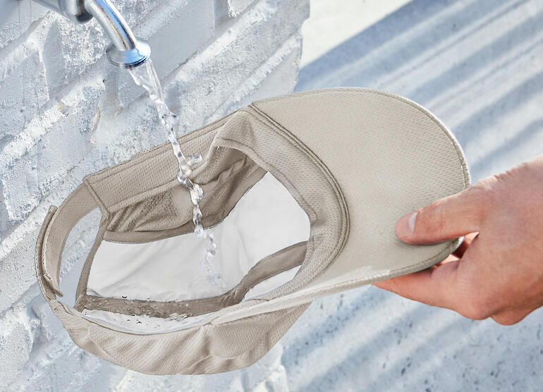 Casquette de refroidissement beige tenue à la main sous l'eau, avec de l'eau qui coule