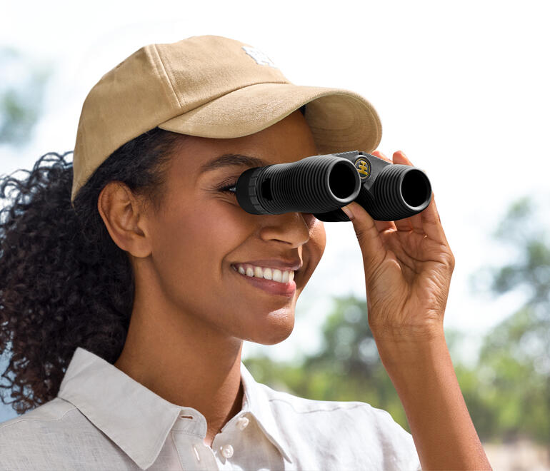 Femme regardant à travers des jumelles compactes dans la nature.