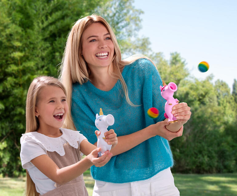 Femme et petite fille rient en jouant avec des ploppers licornes à l'extérieur.