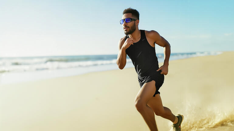 Homme en tenue de sport courant sur la plage avec des lunettes de lumière.