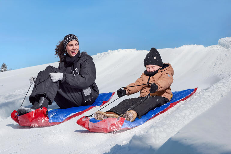 Femme et enfant glissant sur des traîneaux XL dans la neige.