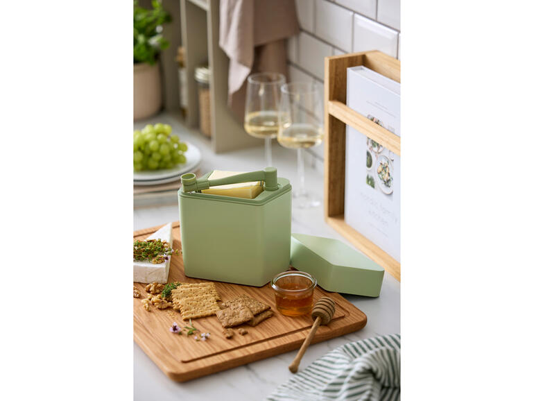 Boîte de fraîcheur pour fromage avec coupeur sur une planche en bois à côté de crackers et de miel.