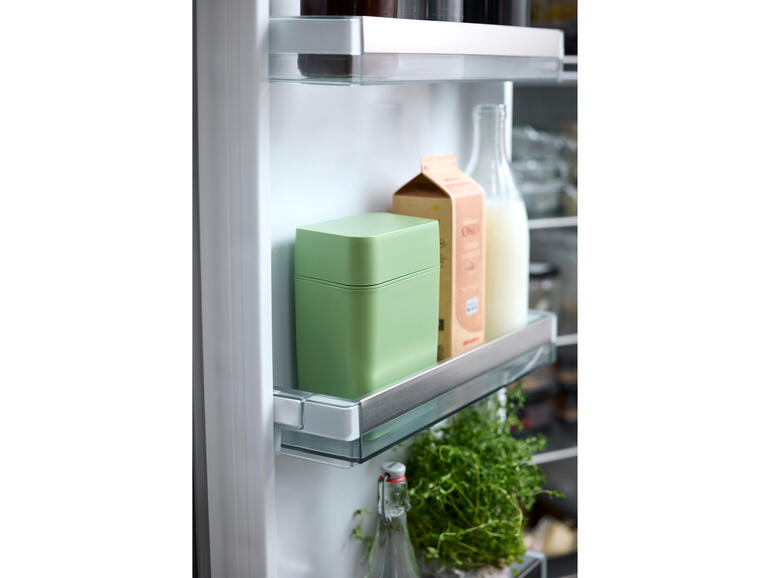 Boîte de fraîcheur pour fromage dans le réfrigérateur, entourée de lait et d'herbes.