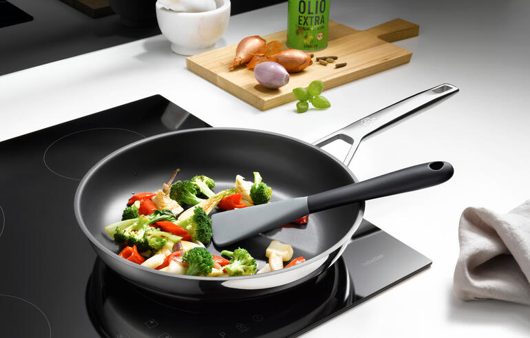 Spatule en silicone flexible dans une poêle avec des légumes mélangés.