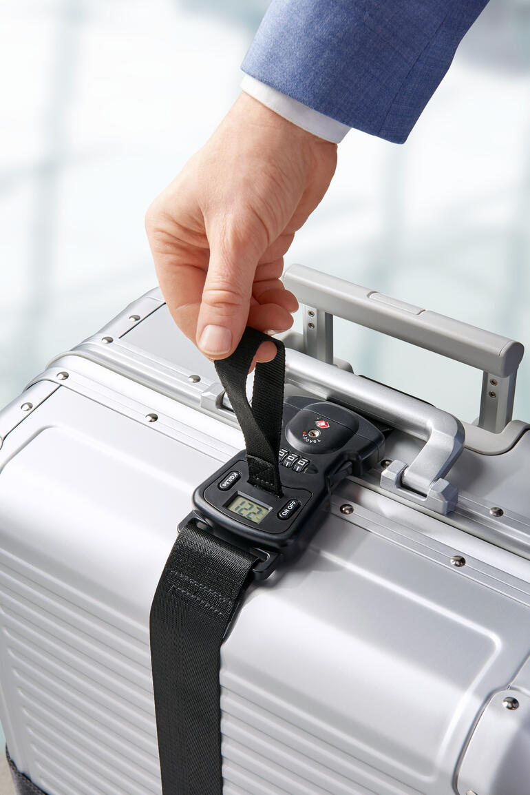 Personne fixant une ceinture de bagage à une valise argentée à l'aéroport.