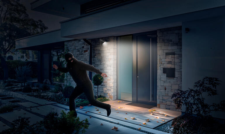 Homme tentant de cambrioler une maison dans l'obscurité alors qu'une imitation de caméra solaire éclaire.