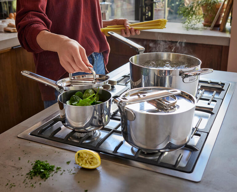 Set de casseroles avec poignée pliable, une casserole et deux casseroles avec des légumes sur la cuisinière.