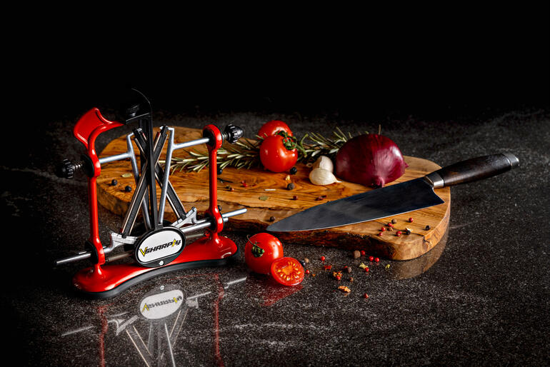 Aiguiseur de couteaux professionnel rouge à côté d'ingrédients frais sur une planche à découper.