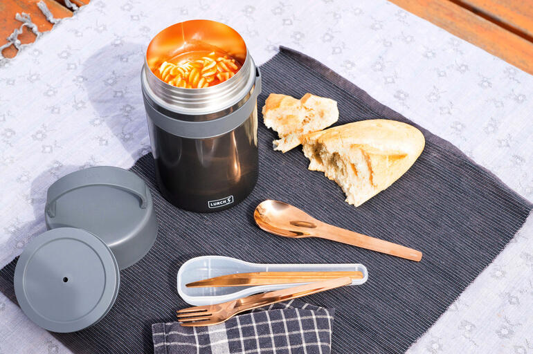 Boîte à snacks noire ouverte avec des pâtes fraîches et du pain sur une table.